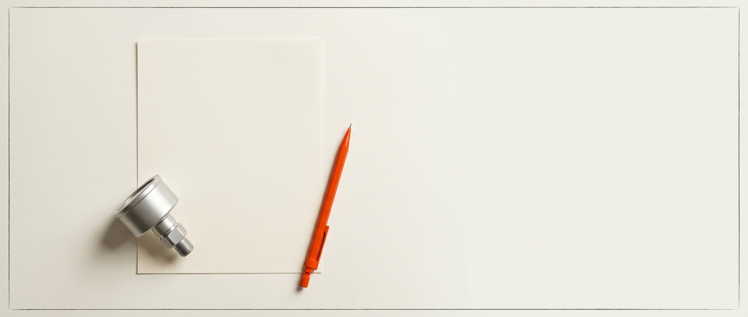 Blank sheet of paper with a machined component as a paperweight and an orange pencil